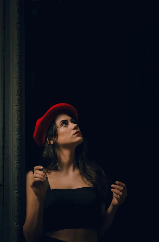 a young woman wearing a hat standing against a wall