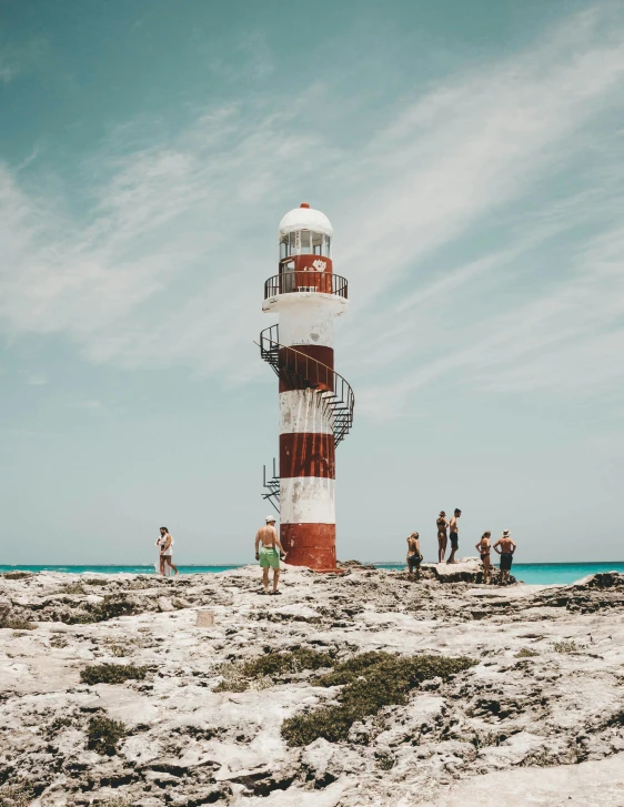 many people are gathered around a red and white lighthouse on the beach