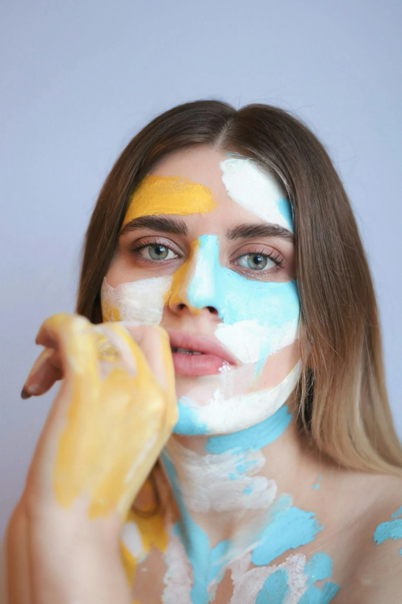 woman with colorful face paint holds banana up to her cheek