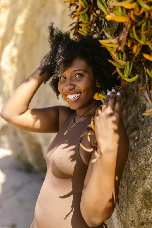 a smiling woman in her bathing suit leaning against a large rock