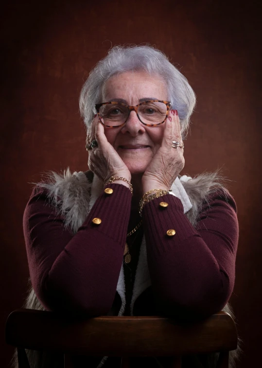 an elderly woman poses for a portrait while wearing glasses and a sweater