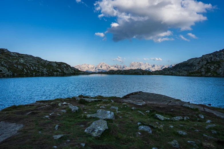 a blue lake with mountains behind it and grass on the other side