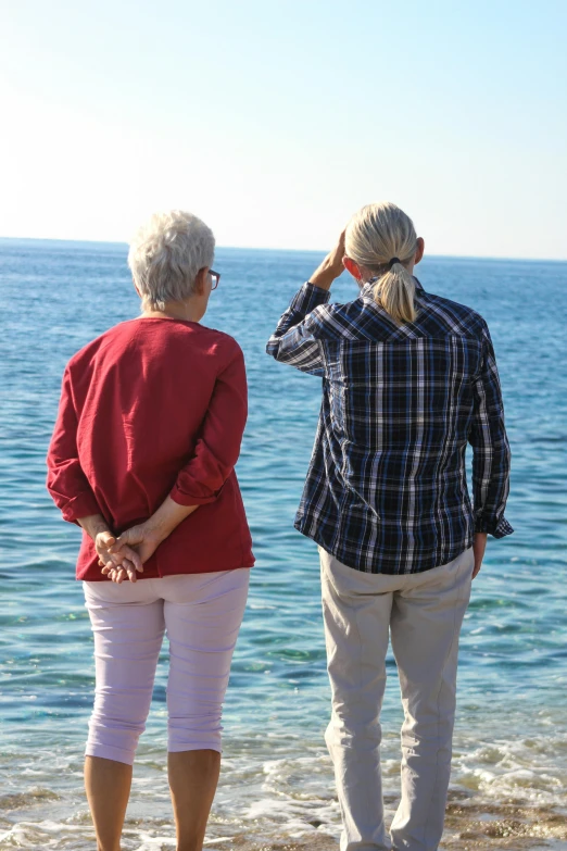 two people standing in the sand looking out into the water