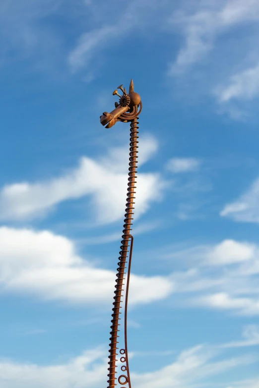 a tall metal sculpture next to blue sky and clouds