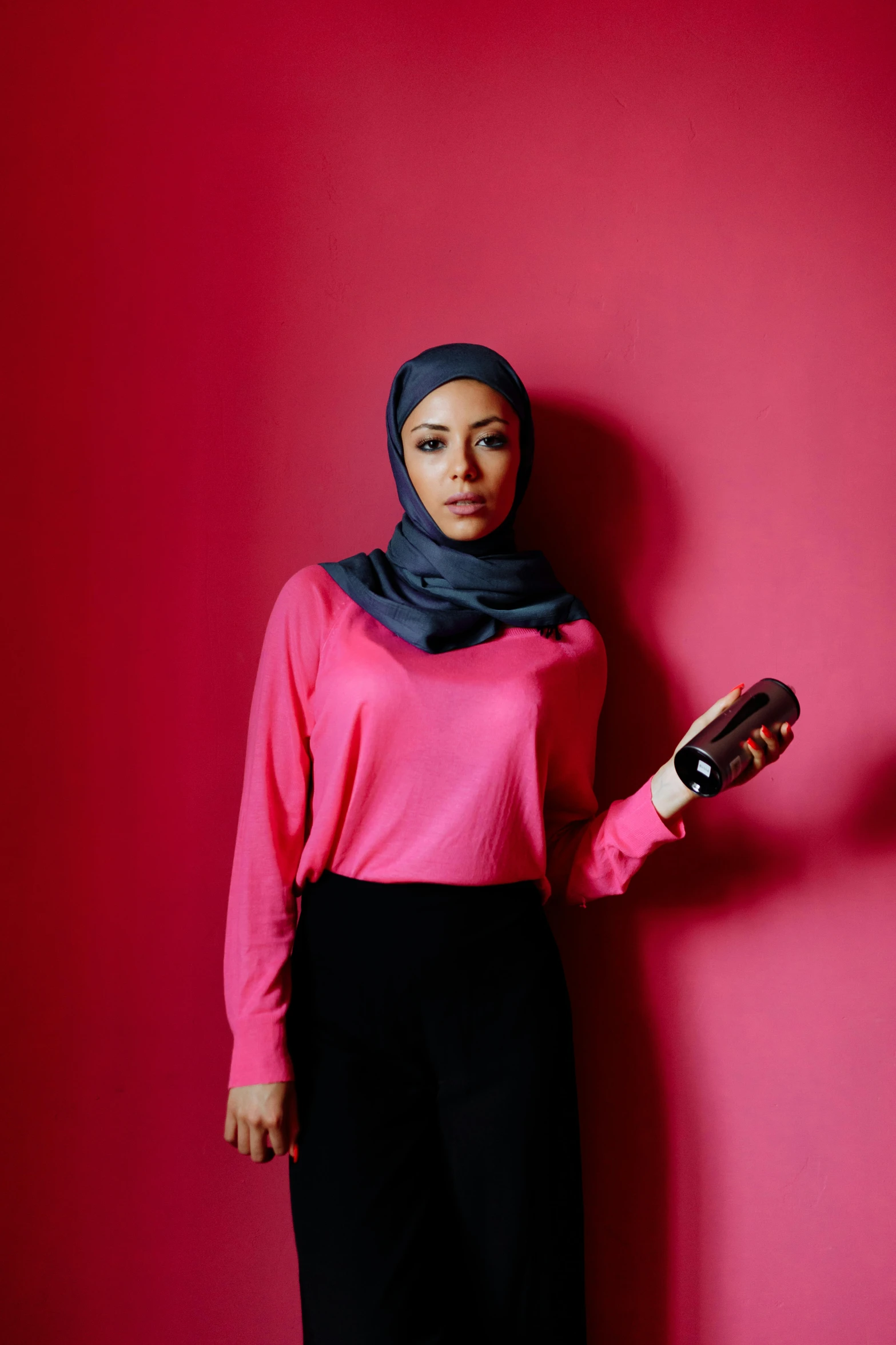 a woman with a long scarf standing against a pink wall