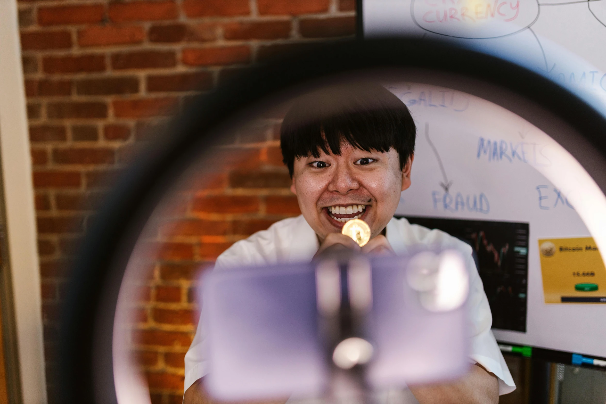 a smiling person holding a device in front of a brick wall