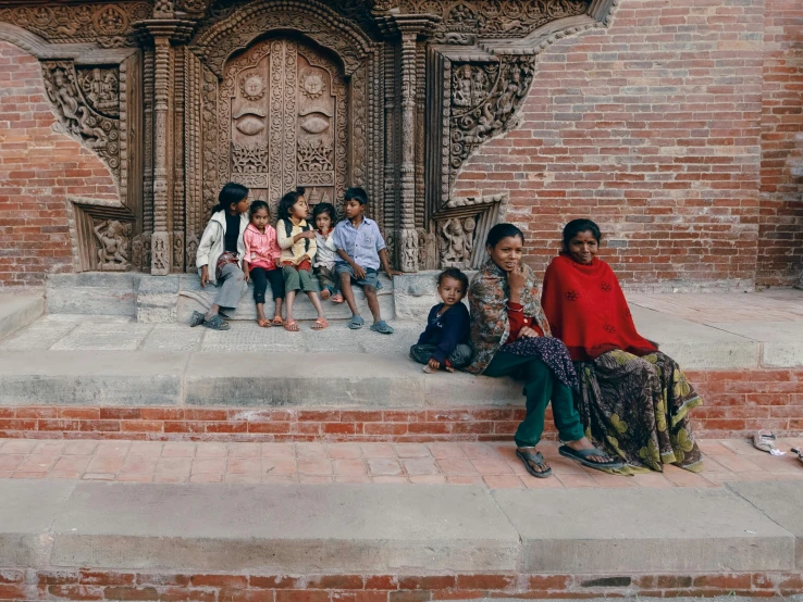 a group of young children sit on the stairs in front of an ornate doorway