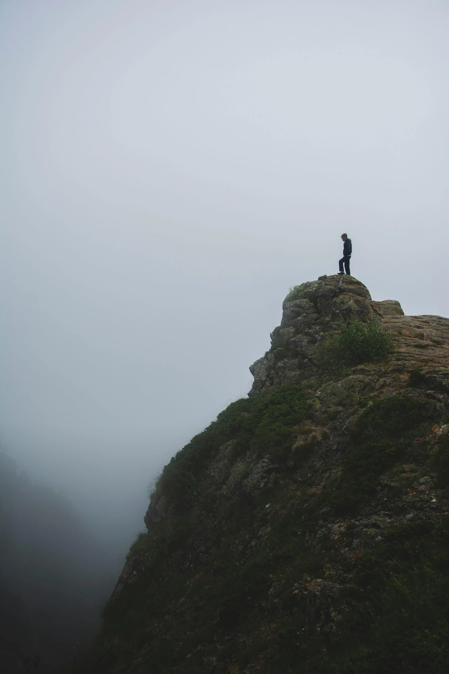 a man on a mountain summit looking up at a foggy sky