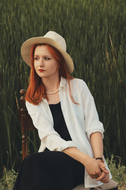 a red haired woman sitting in a chair in front of a wheat field