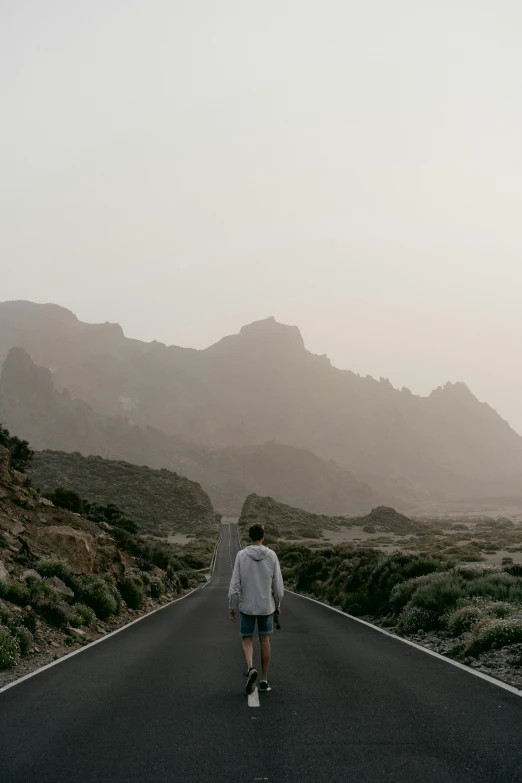 man walking down the middle of road through desert