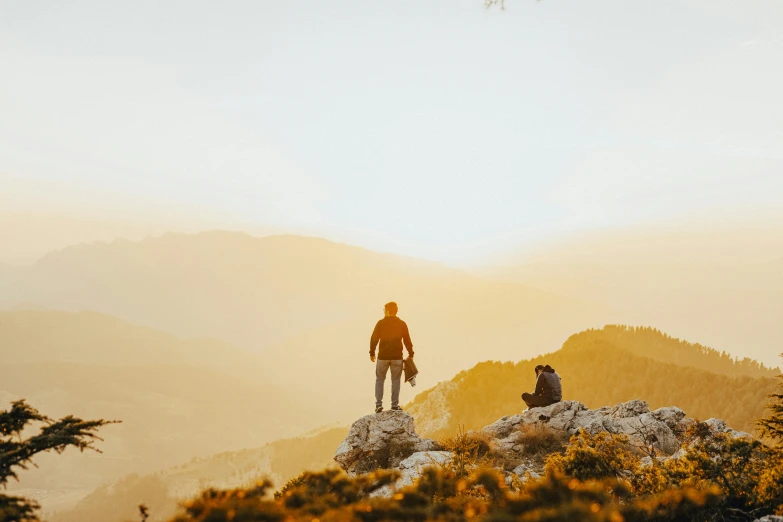 two people standing on top of a mountain during sunset