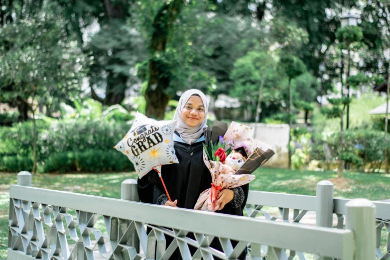 a woman smiles behind a white fence holding flowers