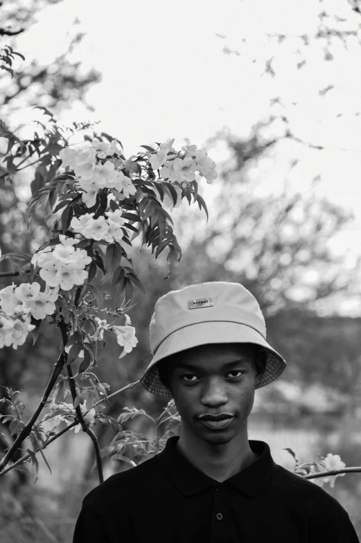 a young man in a hat and black shirt is next to trees