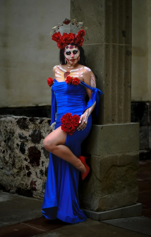 a woman in a blue costume and face makeup sitting against a column