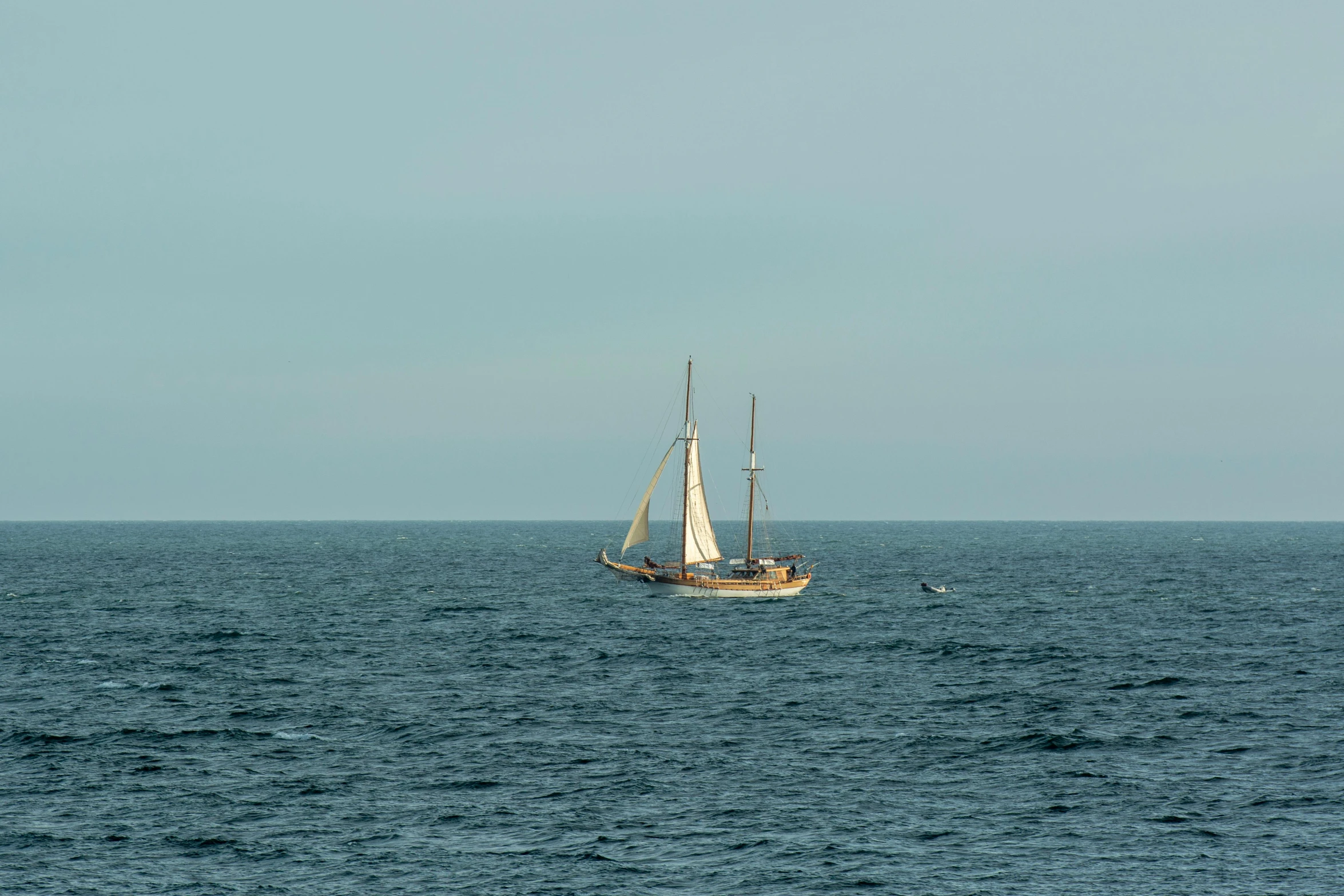 a sail boat sailing on the water with a hazy sky in the background