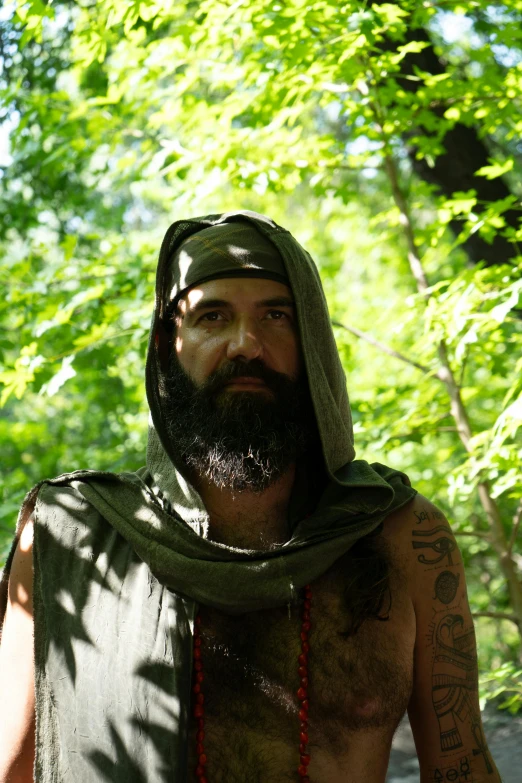 a man with tattoos and a hood on is walking through a forest