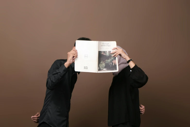 two people holding a book over their eyes