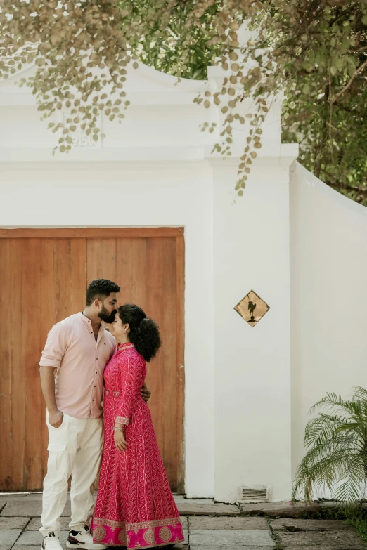 an indian man and woman are cuddling in front of the entrance to a white building