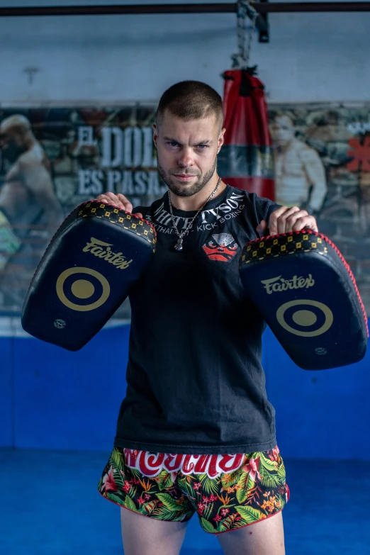 a young man wearing a pair of wrestling trunks holds his pads