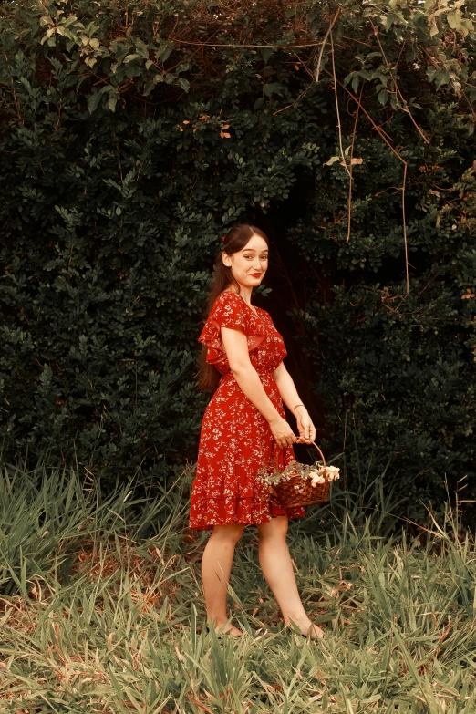 a woman in a red dress holds a basket and stands in tall grass