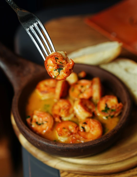 a bowl with shrimp and bread in it being held by a fork