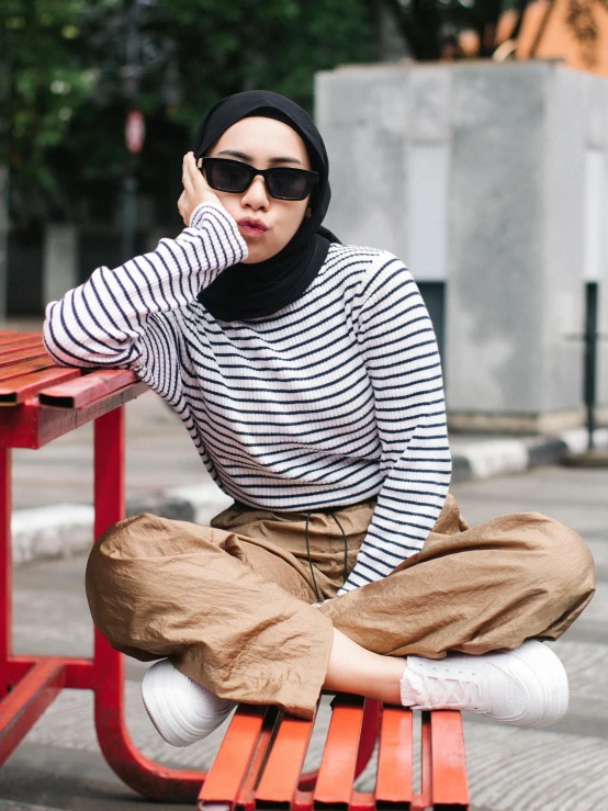 a woman in glasses and head scarf is sitting on a bench