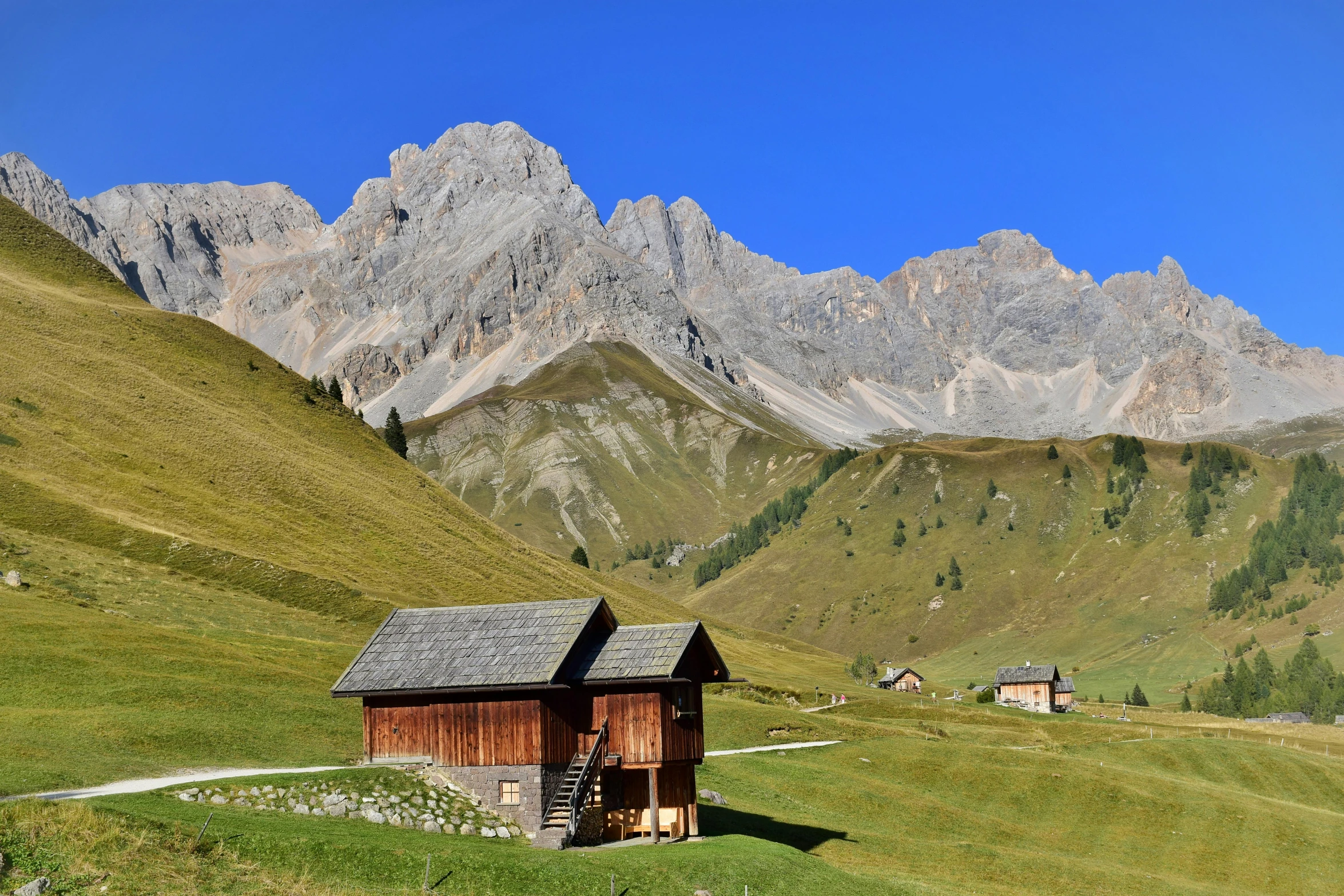 a small hut on the side of a hill with mountains in the background