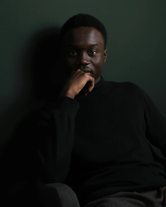 a man poses for a po in front of a dark green wall