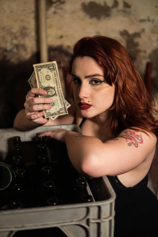 woman with red hair posing at table holding onto a stack of money