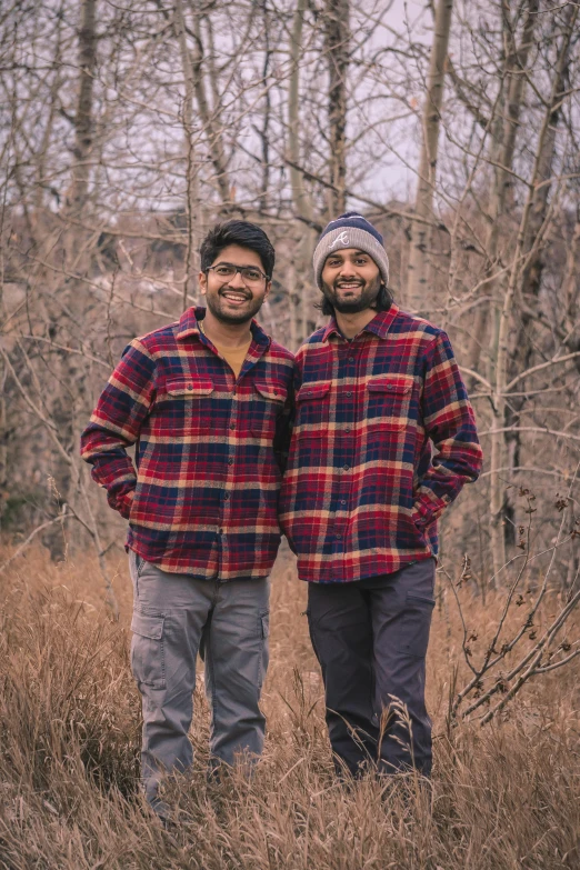 two men standing in front of some trees wearing jackets