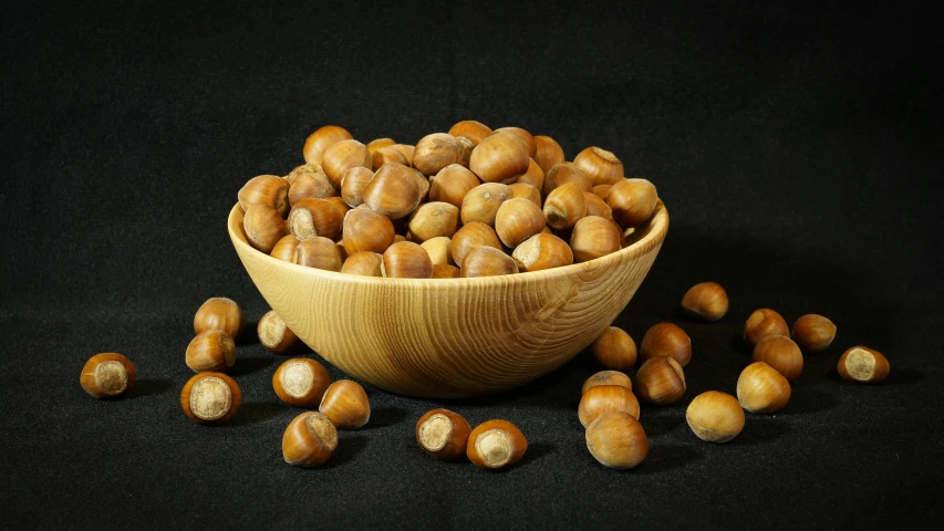 a wooden bowl filled with nuts with dark background