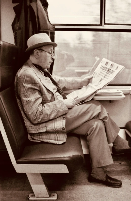 black and white pograph of man on train reading the newspaper