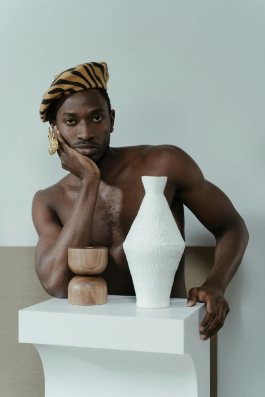 a man sitting on a white table next to a white vase and an empty cup