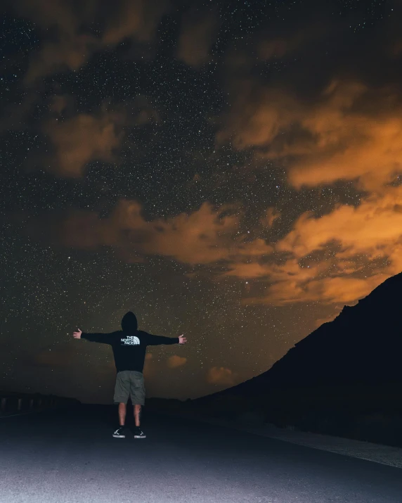 a man is standing on a road at night with his arms wide open