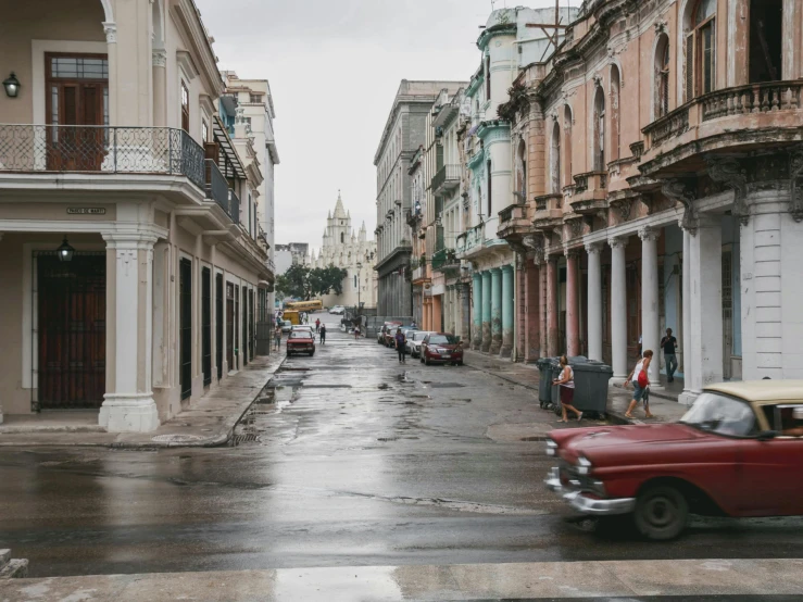 an old red car and some buildings on a rainy day