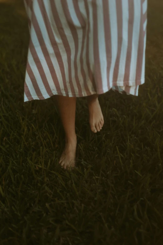 a woman in dress walking in grass with her feet up