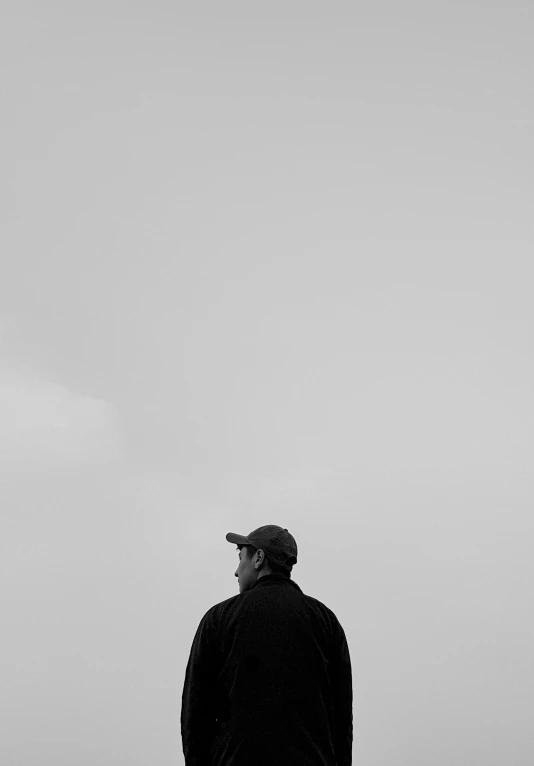 a man standing on the edge of the beach looking at a kite in the sky