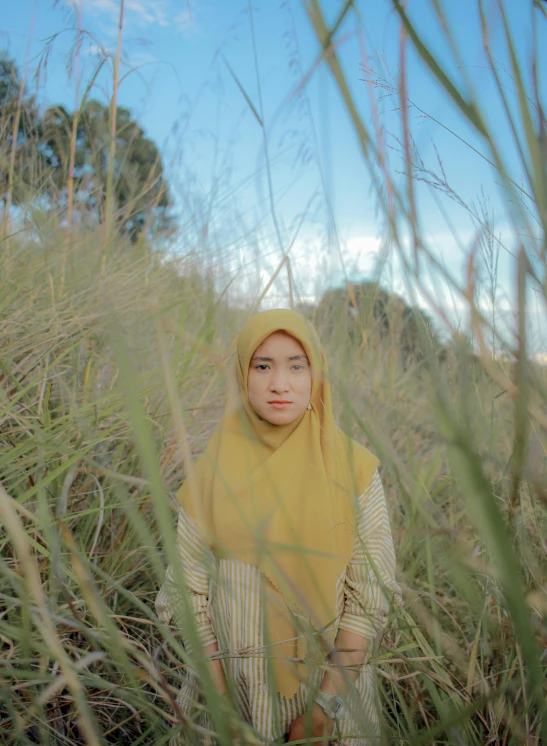 a woman in a yellow headscarf is standing through tall grass