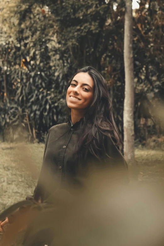 the woman smiles while standing outside by a tree