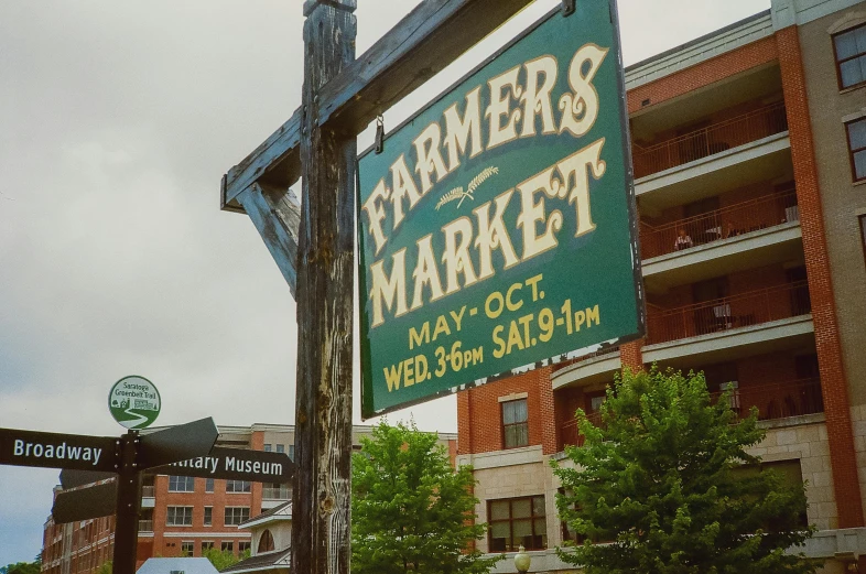 a sign for farmer's market stands in front of brick buildings