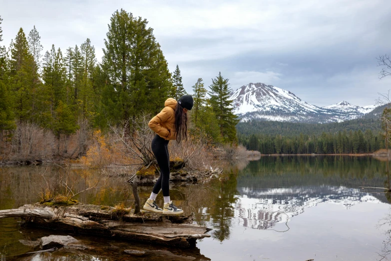 a person on the edge of a river standing next to a tree covered mountain