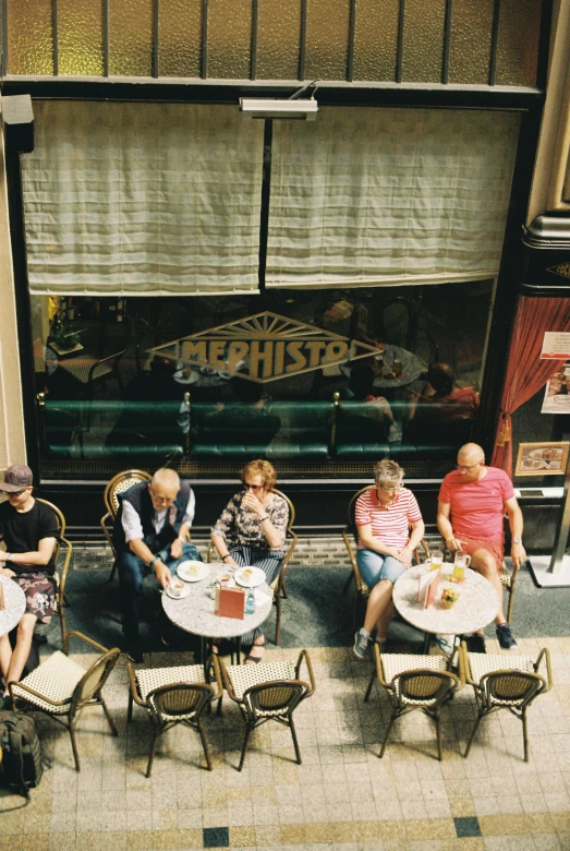 group of people sitting at small tables in front of a store