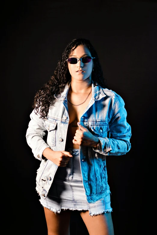 a woman poses in sunglasses and denim jacket