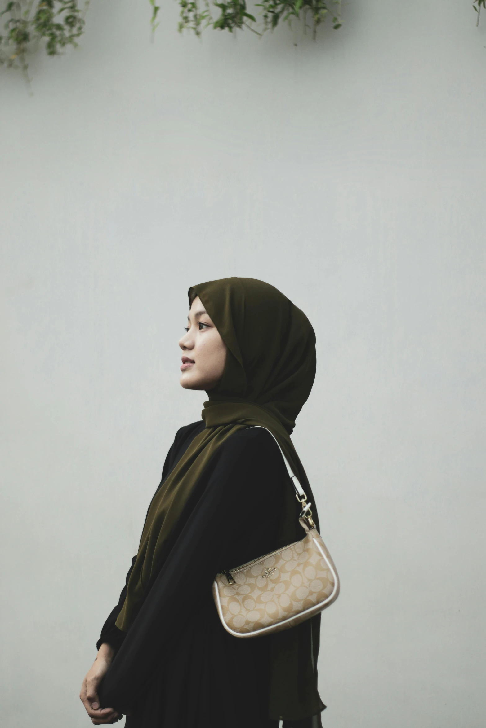 a woman wearing a green hijab holding a brown and white purse