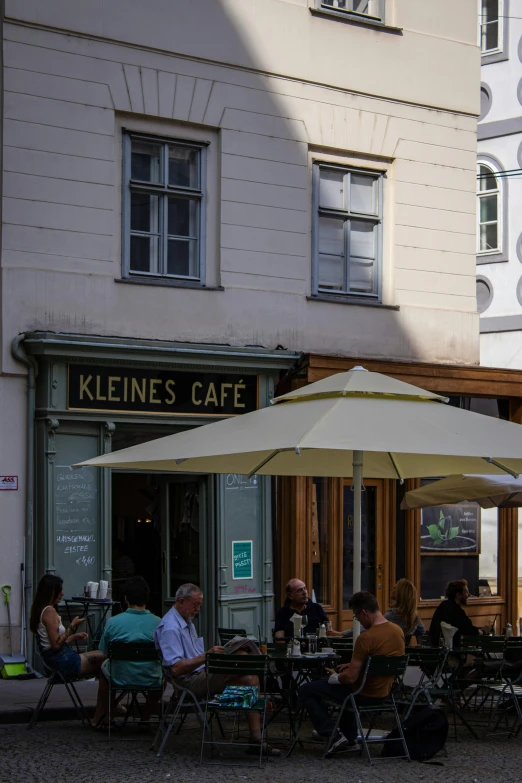 people sitting at tables under an umbrella outside of a cafe