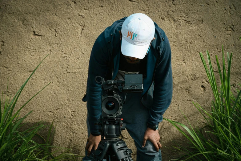 man with camera holding camera near bushes by wall