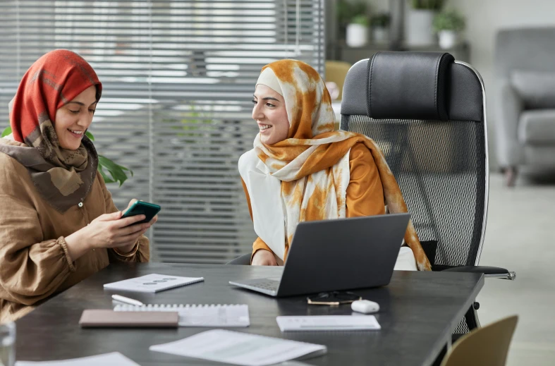 two women sit at a desk on their phones