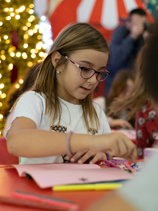 a little girl wearing glasses and writing a letter at a table