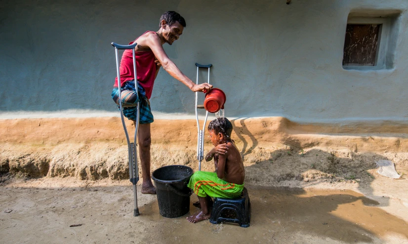 a boy getting a drink from a bottle in a bucket next to an old man sitting on a stool