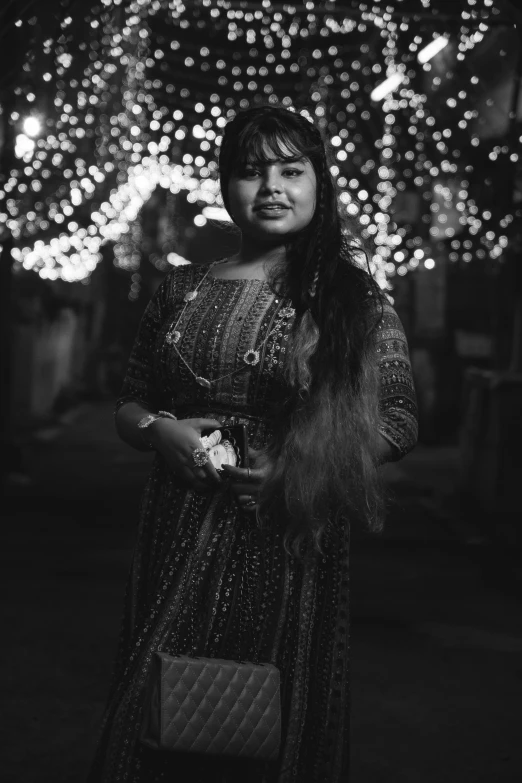 black and white image of woman in dress, holding handbag, standing outdoors at night